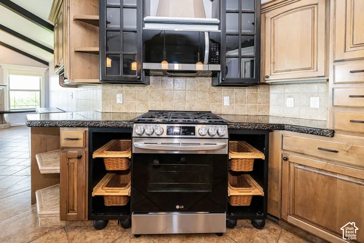 Stainless steel range and overhead microwave, tile backsplash, stone-finish countertops, and varied cabinetry with glass-paneled accents