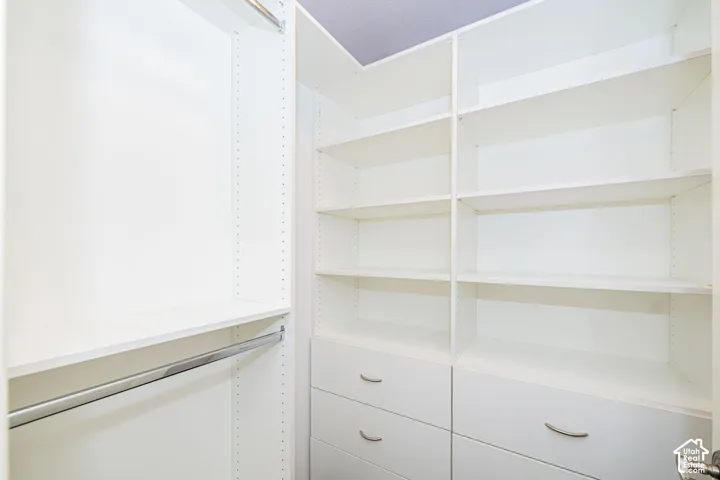 Integrated closet organization system featuring white shelving, multiple hanging rods, and built-in drawers with brushed nickel hardware