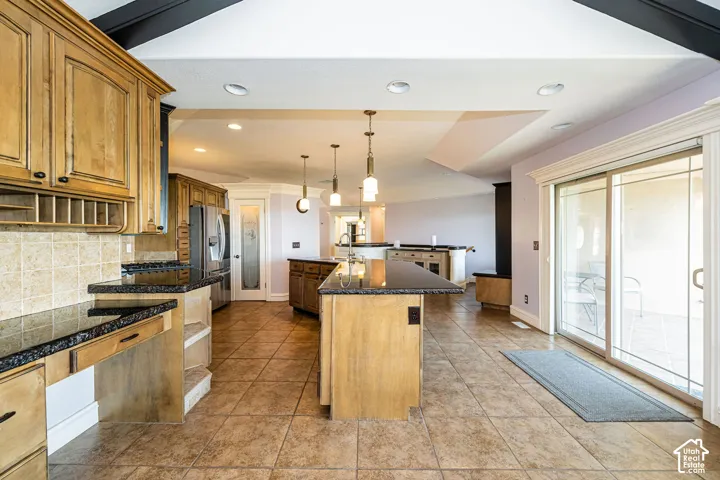 Spacious kitchen featuring light wood cabinetry, dark granite countertops, tile flooring, a two-tiered island with pendant lighting, and sliding glass doors