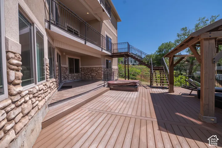 Third Level Balcony walkout. Expansive composite decking featuring a built-in hot tub, a wooden gazebo structure, and a multi-level exterior staircase with metal railings