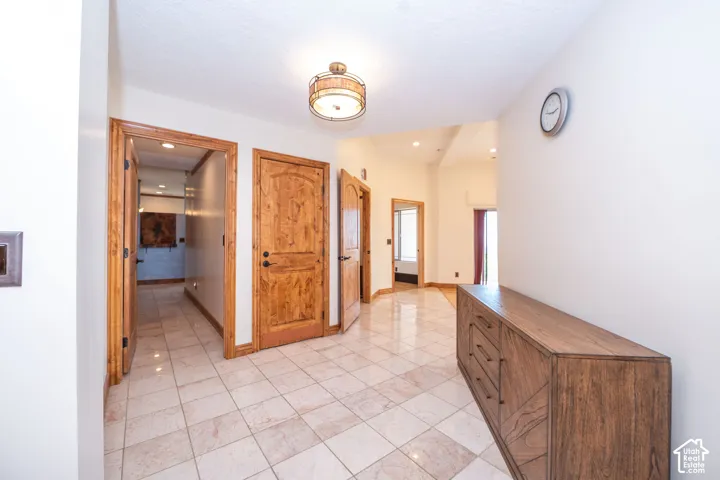 Spacious hallway featuring light-toned tile flooring, recessed lighting, and a modern drum light fixture