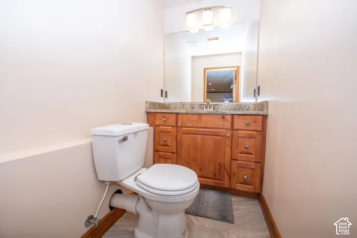 Compact bathroom featuring a wood-finish vanity with a stone countertop, a wall-mounted mirror, and a three-light vanity fixture