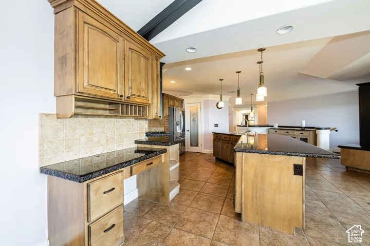 Spacious kitchen featuring an expansive island, granite countertops, wood cabinetry, pendant lighting, and tiled flooring