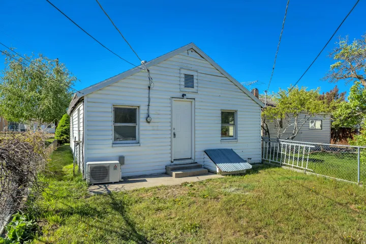Rear exterior featuring white horizontal siding, a gabled roof, and a basement entrance with a metal cover