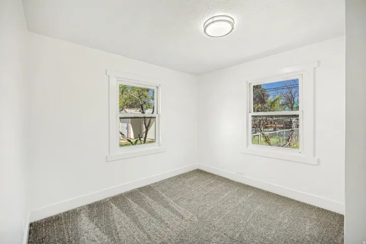 Bright interior space featuring two windows, neutral wall tones, textured gray carpeting, white baseboards, and a contemporary ceiling light fixture