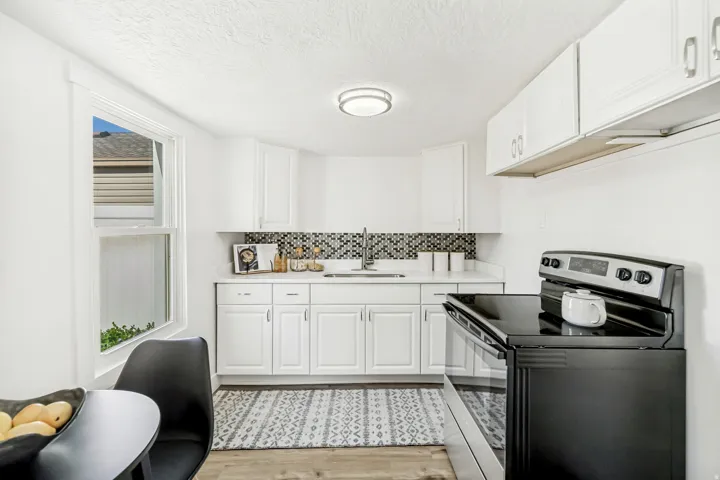 Contemporary kitchen featuring white cabinetry, quartz countertops, a mosaic tile backsplash, and wood-finish flooring