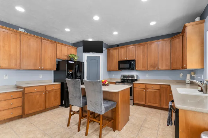 Spacious kitchen featuring an island, light wood-finish cabinetry, tile flooring, recessed lighting, and a composite sink