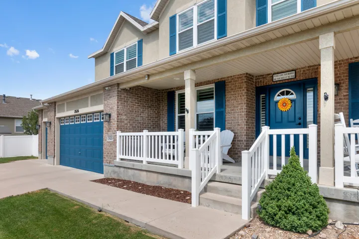 Brick and stucco exterior featuring a covered front porch with white railings, a blue entry door with sidelights, and a blue garage door