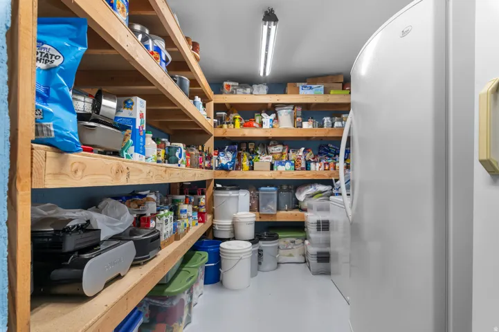 Spacious pantry featuring extensive wood shelving, a durable painted concrete floor, and a white freestanding refrigerator