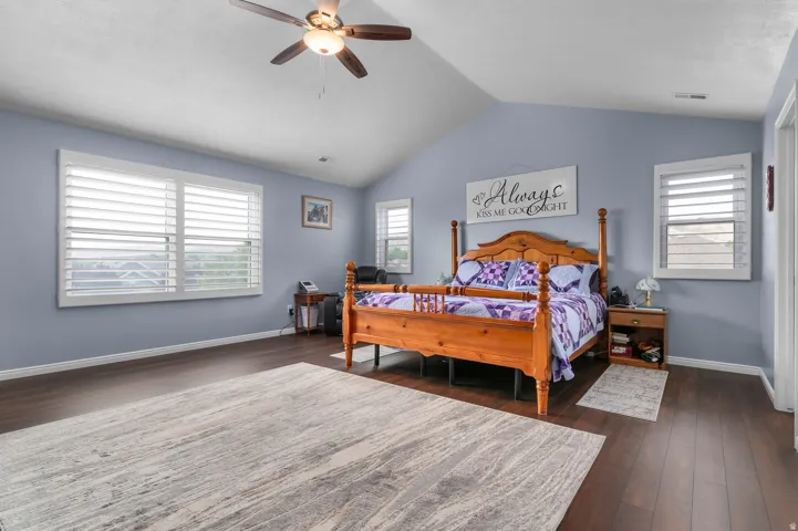 Spacious room featuring vaulted ceilings, wood-finish flooring, multiple windows with white plantation shutters, and a ceiling fan with integrated lighting