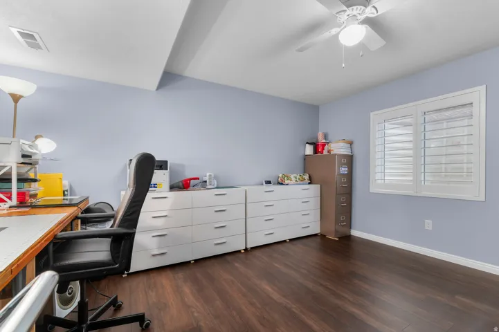 Room featuring wood-finish flooring, a ceiling fan with integrated lighting, and a window with plantation shutters