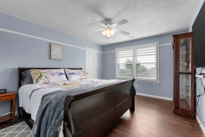 Bedroom featuring wood-finish flooring, a ceiling fan with integrated lighting, and white trim work
