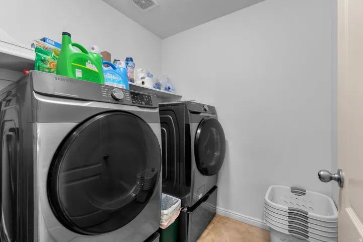 Dedicated laundry space featuring a side-by-side appliance configuration, overhead shelving, light-colored walls, and a vent in the ceiling