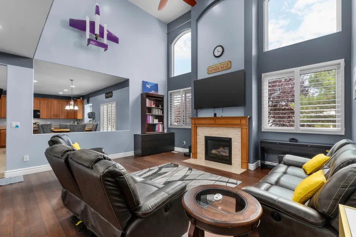 Living area featuring soaring ceilings, wood-finish flooring, a fireplace with a wood mantle and tile surround, and multiple windows with plantation shutters