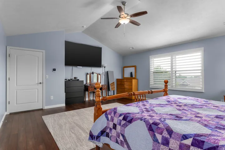 Vaulted ceiling with a ceiling fan, wood-finish flooring, and a window with white louvered shutters
