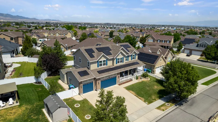 Two-story residence featuring a covered front porch, a two-car garage with blue doors, and solar panels on the roof