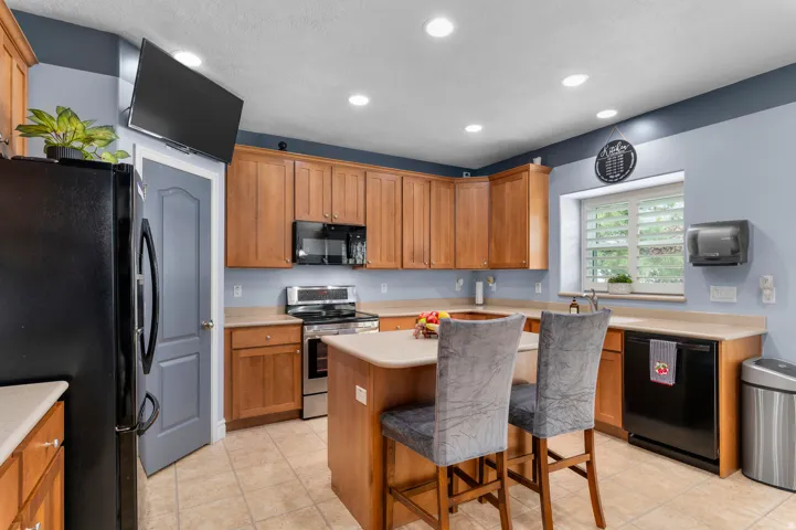 Kitchen featuring wood cabinetry, stainless steel appliances, an island with countertop seating, recessed lighting, and tile flooring