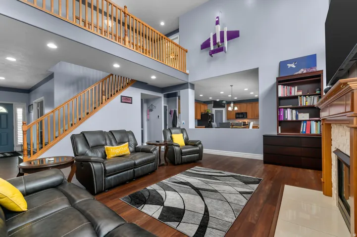 Open-concept living space featuring wood-finish flooring, a two-story ceiling, and a fireplace with a light-toned stone surround