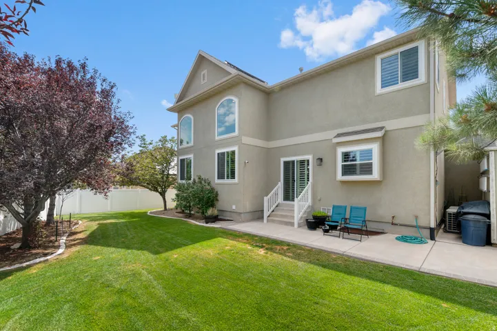 Spacious backyard featuring a manicured lawn, concrete patio, and mature trees