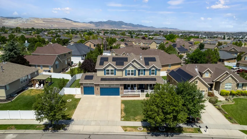 Two-story residence featuring a covered front porch, integrated solar panels, a concrete driveway, and a two-car garage with blue doors