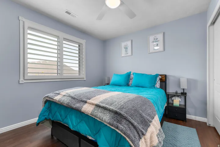 Bedroom featuring plantation shutters, wood-finish flooring, a ceiling fan, and a built-in closet