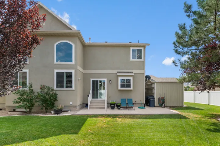Rear exterior featuring a spacious concrete patio, a manicured lawn, and a privacy fence