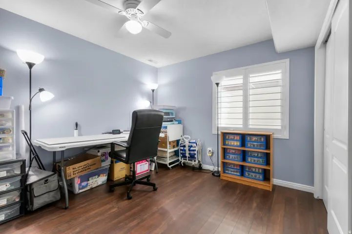 Room featuring wood-finish flooring, a ceiling fan with integrated lighting, and a window with plantation shutters