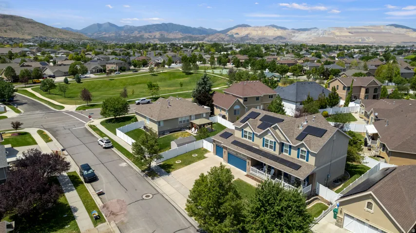 Two-story residential property featuring a neutral-toned exterior, blue-shutter windows, a covered front porch with white railing, integrated solar panels, and an attached three-car garage