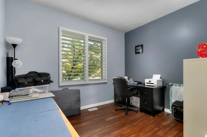Room featuring wood-finish flooring, a white-framed window with plantation shutters, and a two-tone wall treatment