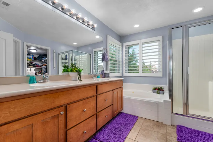 Bathroom featuring a double vanity with wood cabinetry and light-toned countertops, a glass-enclosed shower, and a built-in tub with white surround
