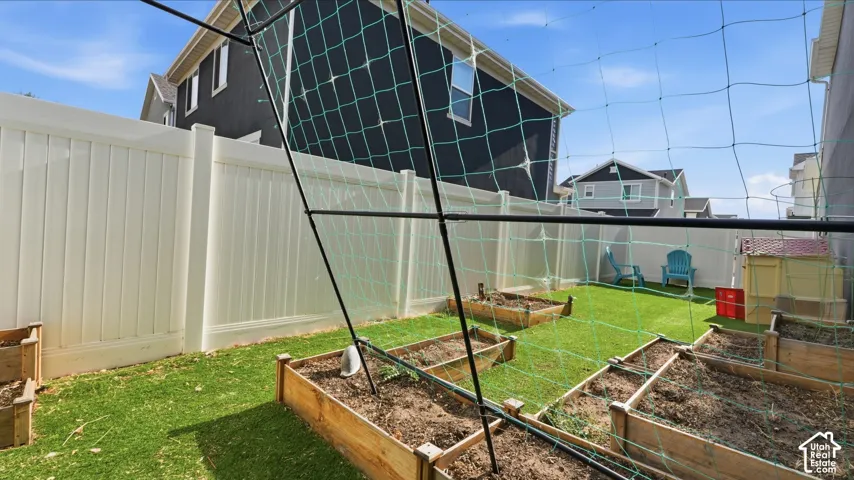 Backyard featuring multiple raised garden beds, artificial turf, and full vinyl fencing for privacy.