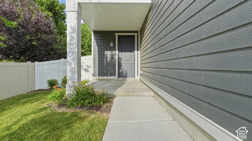 Covered front porch with concrete walkway leading to the entry, framed by white vinyl privacy fencing and lush landscaping along the path.