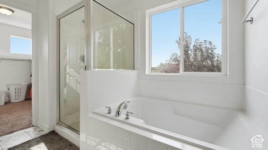 Soaking tub with tile surround beneath a window, alongside a glass-enclosed shower.