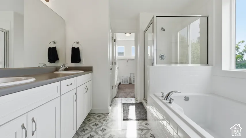 Primary bath featuring a dual-sink vanity, patterned tile flooring, a soaking tub, and a separate glass-enclosed shower.