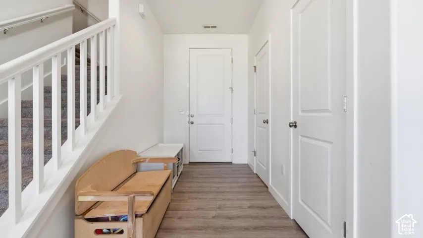 Entryway featuring wood-finish flooring, white paneled doors, and a staircase with white balusters