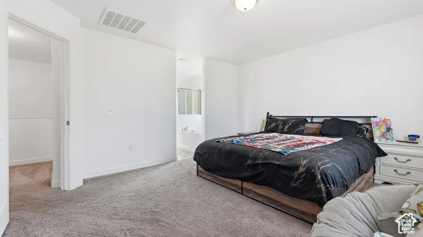 Generously sized primary bedroom with carpet flooring and direct access to the en-suite bathroom.