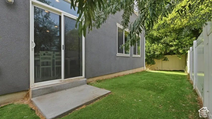 Backyard patio area with sliding glass door access, artificial turf lawn, and mature shade trees along the fence line.