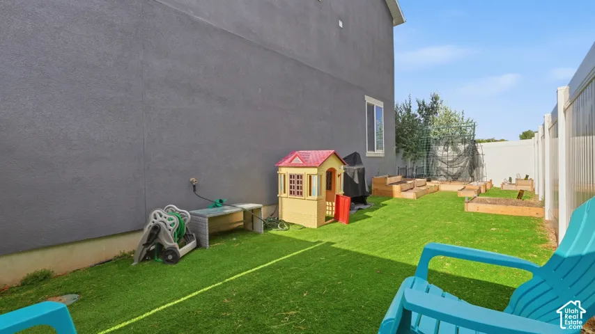 Fenced backyard with artificial turf, raised garden beds, and a gated side yard entrance.