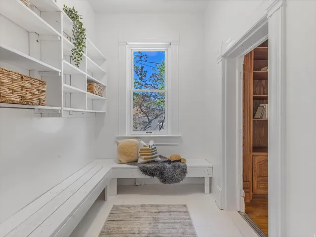 Entryway featuring built-in shelving, white wood-finish flooring, a built-in bench, and a window with trim