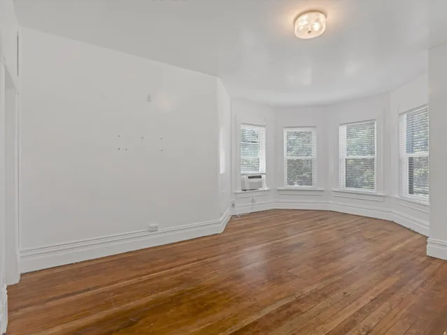 Hardwood flooring throughout a room featuring a bay window with multiple paneled windows, white blinds, and crisp white trim