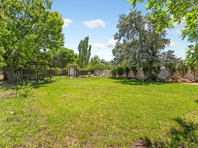 Expansive green lawn with mature shade trees, a perimeter fence, garden arbor, and a fire pit area