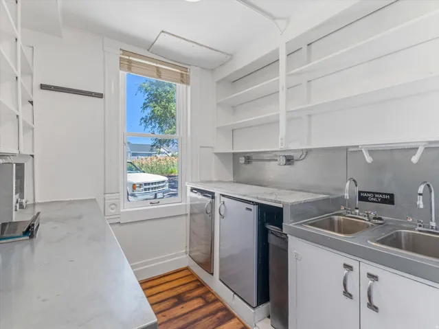 Functional utility space featuring a double-basin stainless steel sink, stainless steel countertops, built-in open shelving, and wood-finish flooring