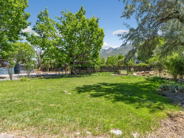 Expansive grassy yard area featuring mature trees, a wood privacy fence, and mountain scenery