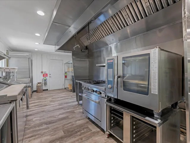 Commercial-grade kitchen featuring stainless steel appliances, extensive stainless steel counters, a large professional range with a powerful ventilation hood, and recessed lighting