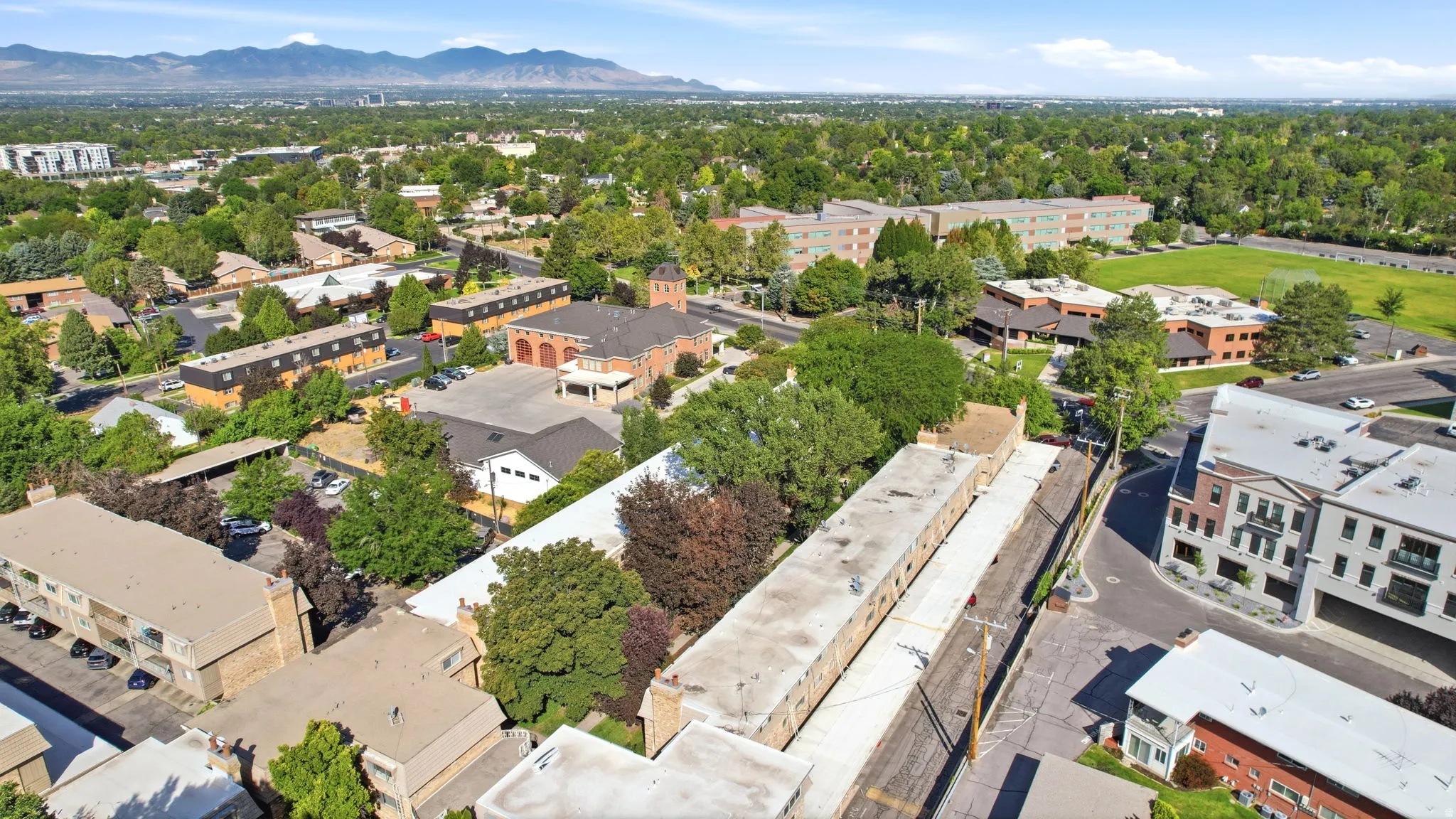 Aerial perspective showcasing a mixed-use neighborhood with established trees, multi-story buildings, and a clear mountain backdrop