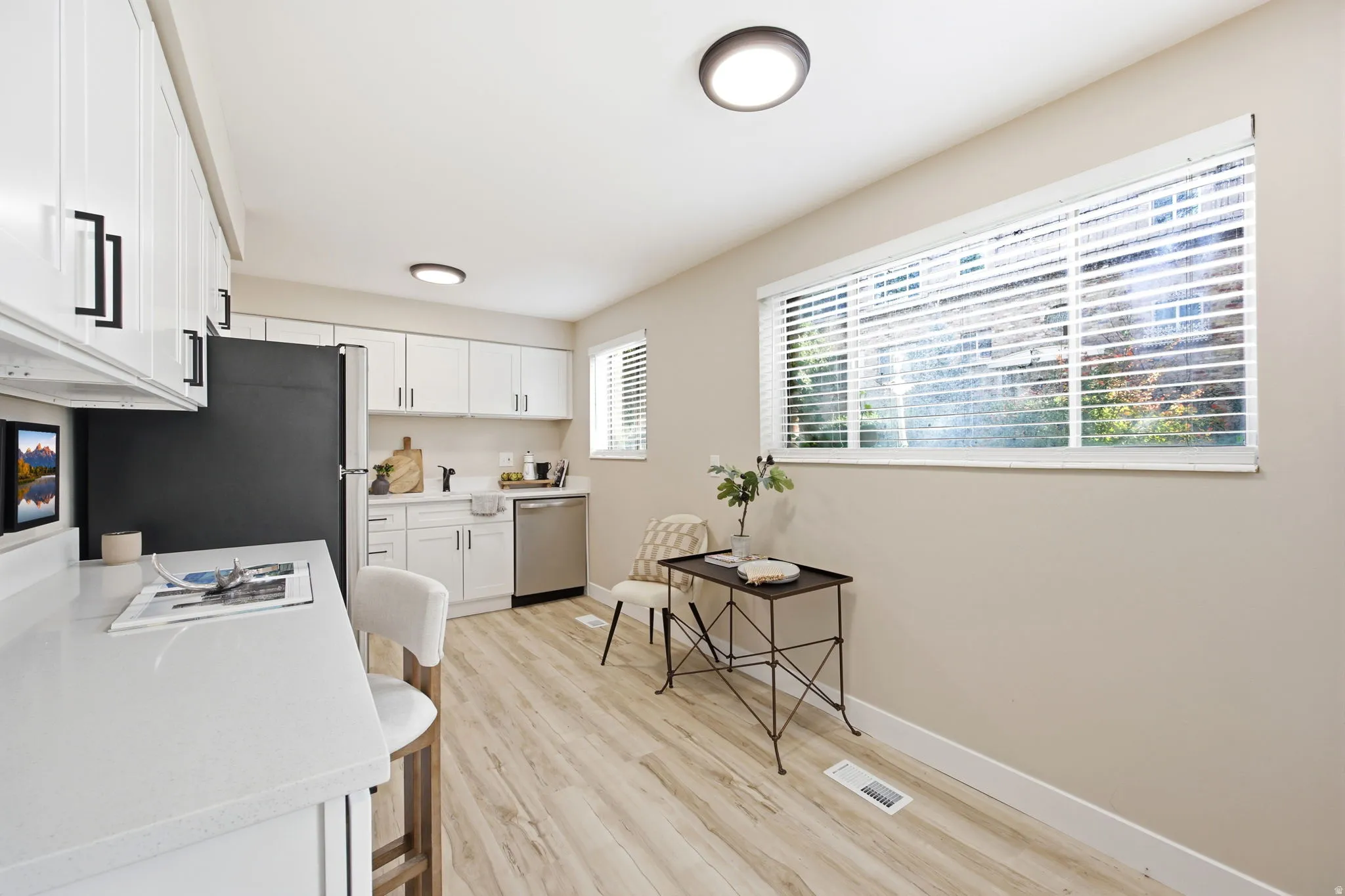 Bright kitchen featuring white cabinetry, light countertops, stainless steel appliances, and wood-finish flooring