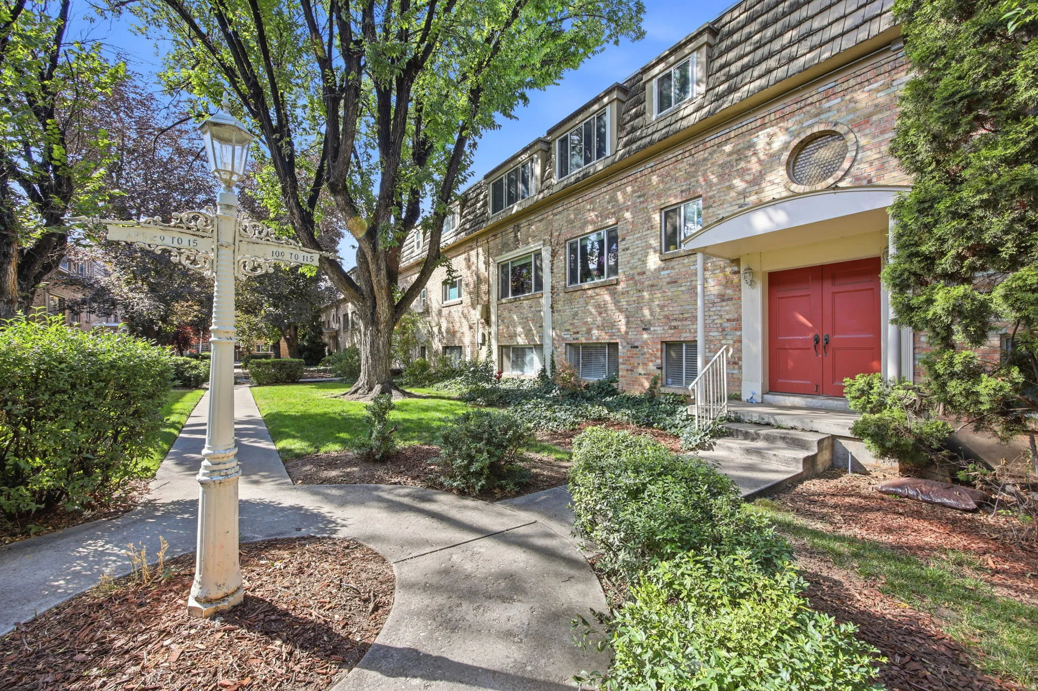 Brick facade building featuring a prominent red double-door entry with arched portico, a round architectural window, and a shingled mansard roof