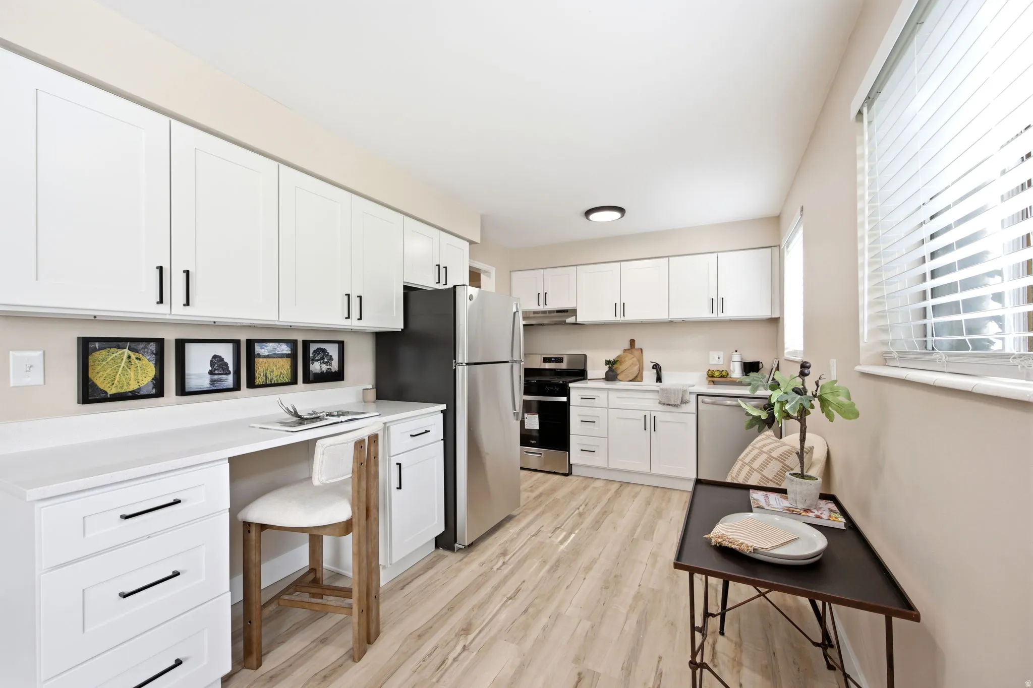 Modern kitchen featuring white shaker cabinetry with matte black hardware, light wood-finish flooring, stainless steel appliances, and solid surface countertops