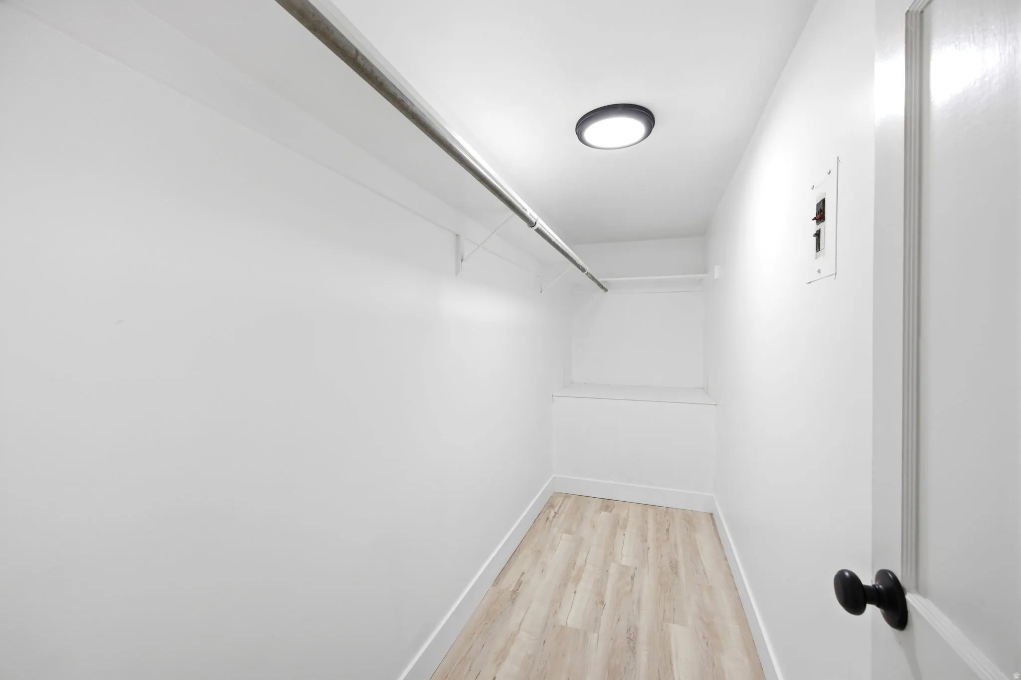 Walk-in closet featuring light wood-finish flooring, white walls, and a ceiling-mounted light fixture