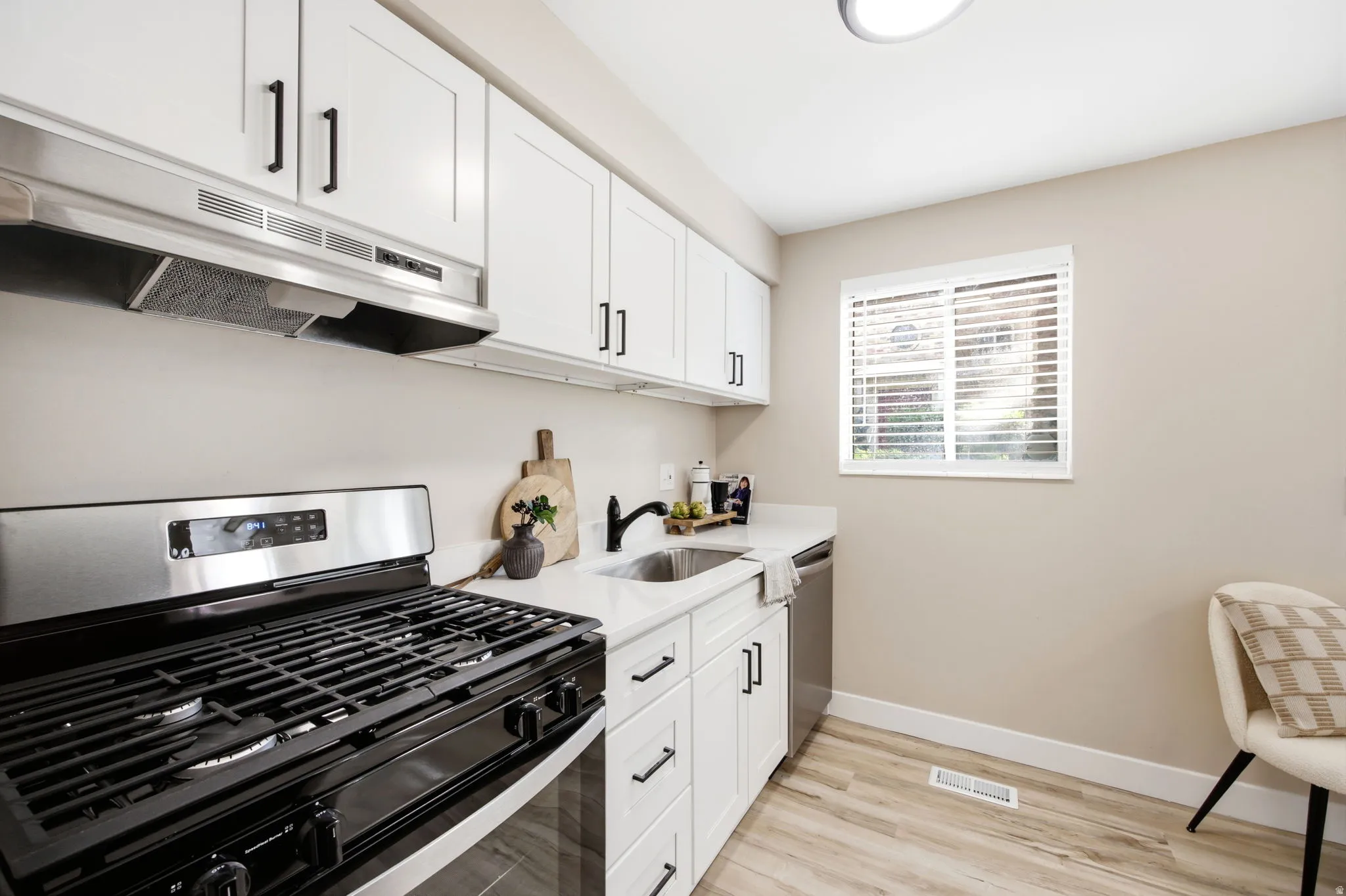 Kitchen featuring white cabinetry, a stainless steel range hood, a black gas range, white countertops, and wood-finish flooring